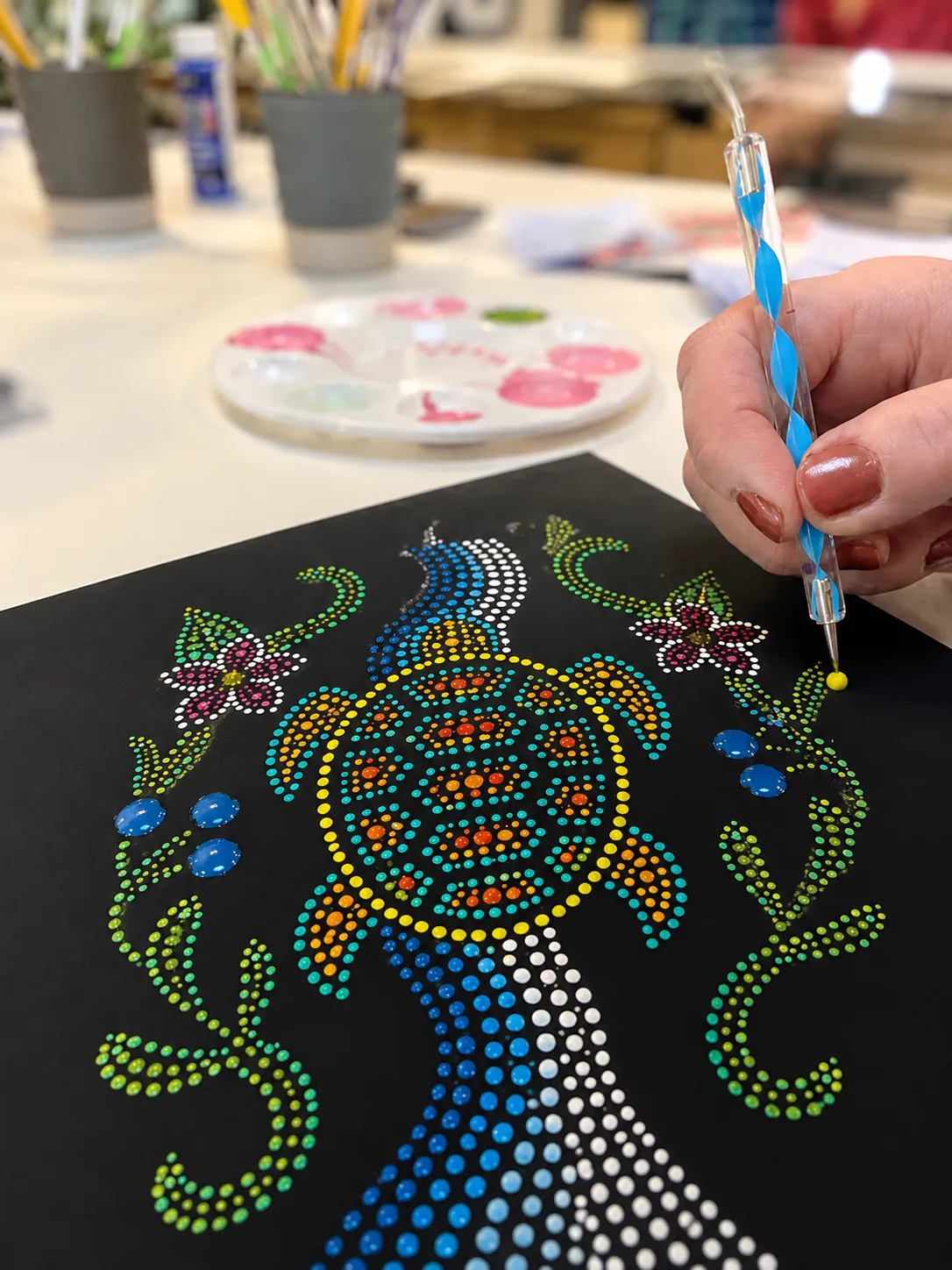 Hand dotting a turtle design with a blue dot pen